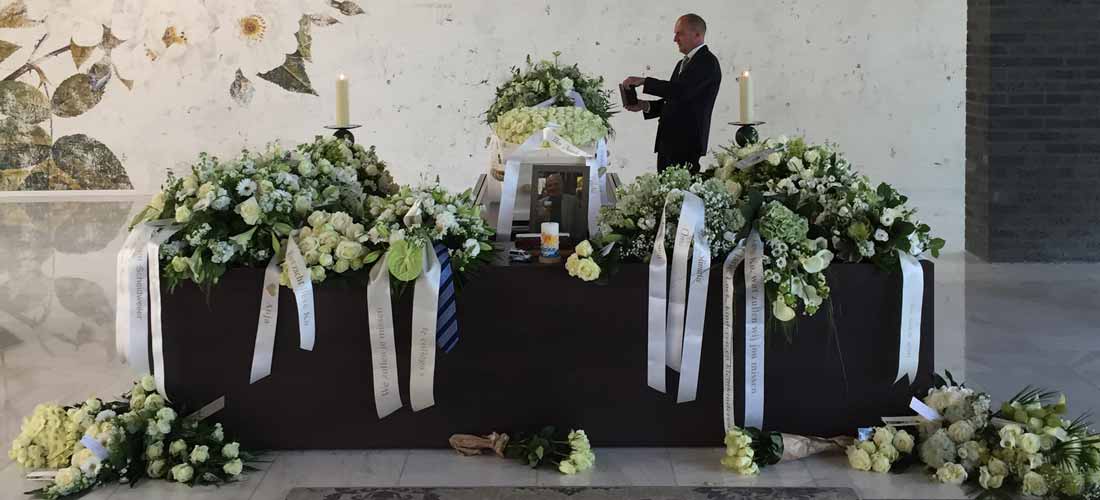 Uitvaartverzorger maakt een foto bij het afscheid van alle bloemstukken en linten in de aula van crematorium Westgaarde.