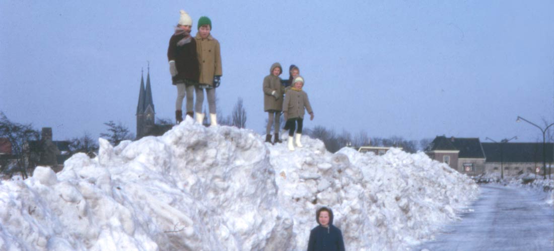 Kinderen in Duivendrecht die bovenop een berg sneeuw staan met op de achtergrond de Sint-Urbanuskerk.